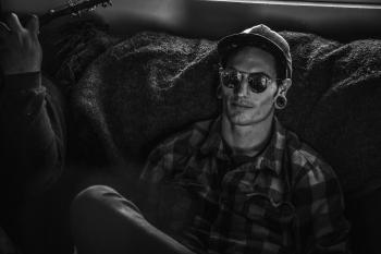 Grayscale Photo of Man Wearing Snapback Cap and Plaid Dress Shirt Sitting on Couch