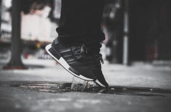 Grayscale Photo of Person Wearing Adidas Nmd Jumping on Puddle