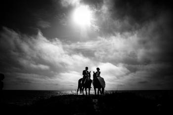 Grayscale Photography of Couple Riding on Horse With Body of Water and Sky As Background