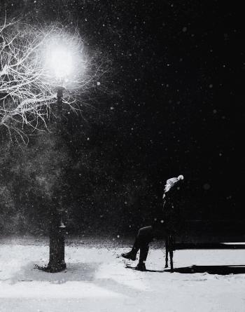 Grayscale Photography of Person With Knit Pompom Cap Sits in Front Turned on Light Post at Night