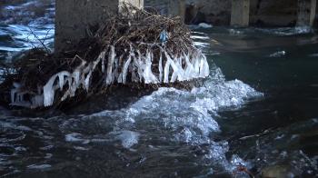 Frozen stream. Snowy and icy stones in water. Icicle bellow ...