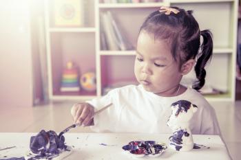 Child painting, little girl having fun to paint on stucco doll o ...