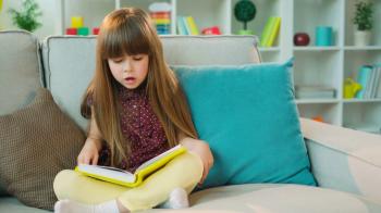 Beautiful little girl reading book and thinking, looking at the ...