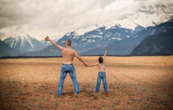 Man and a Boy in Blue Denim Jeans Standing in Brown Open Space Near White and Gray Snowy Mountains during Daytime