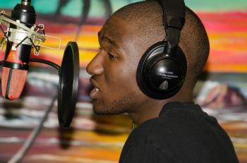 Man in Black Tops Wearing Black Headphones Singing in Front of Black Condenser Microphone