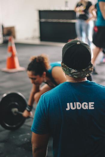 Man in Blue Crew-neck Shirt Staring At Woman Trying To Lift Barbell