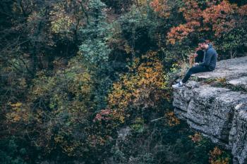 Man In Hoodie Sitting On Rock Cliff