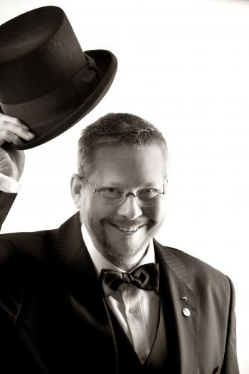 Man in Tuxedo and Eyeglasses Holding Top Hat in Grayscale