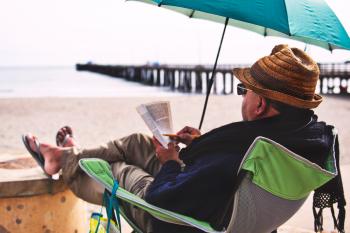 Man Sitting on Chair Under Blue Umbrella Near Beach