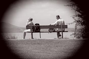 Man Sitting on Other Edge of Bench Parallel to Woman With Bags in Between Them