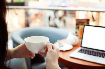 Person Holding White Ceramic Teacup in Front of a Macbook Pro