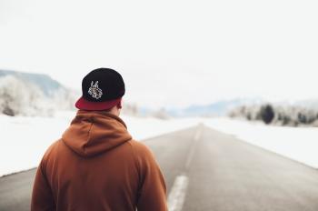 Person in Brown Hoodie and Fitted Cap Walking on Road