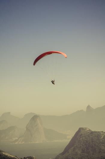 Person in Parachute Gliding Above Mountains