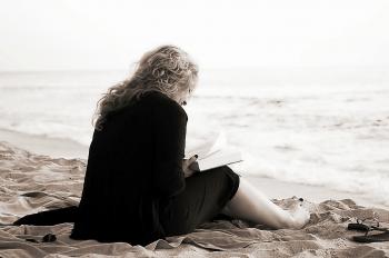 Person Sitting on the Seashore While Reading a Book