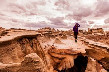 Person Walking on Rock Formation Under Cloudy Sky