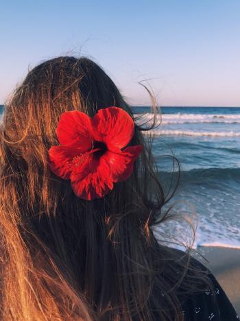 Photo of a Woman With Hibiscus on Her Head Facing Towards the Sea