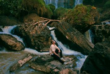 Photo of Man Sitting on Gray Rock Surrounded by Water Falls