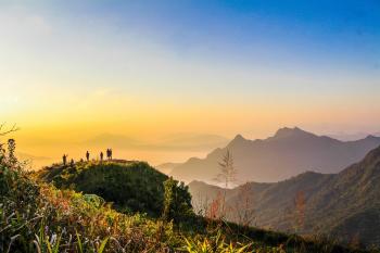 Photo of People Standing on Top of Mountain Near Grasses Facing Mountains during Golden Hours
