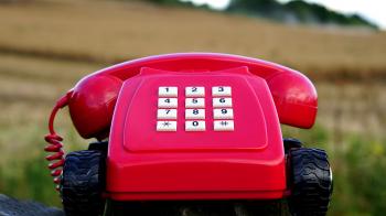 Red Rotary Phone With Black Wheels Near Brown Grasses during Day Time