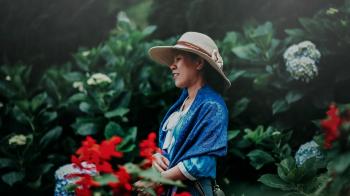 Selective Focus Photo of Woman in Blue Shawl and Brown Sun Hat in the Middle of Garden