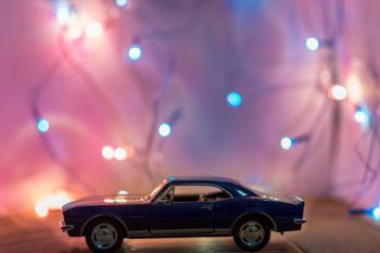 Selective Focus Photography of Classic Blue Coupe Die-cast Model in Front of String Lights on Table
