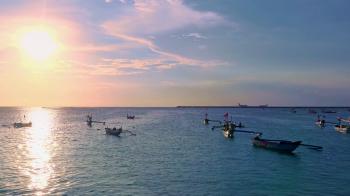 Outrigger fishing boats floating in ocean lit by setting sun against ...
