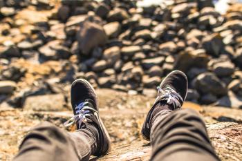 Shallow Focus Photography of Person Wearing Gray Jeans Sitting in Front Rocks