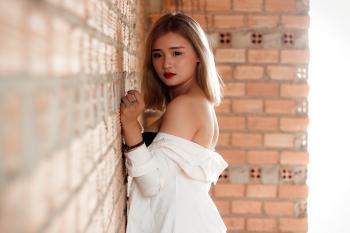Shallow Focus Photography of Woman in White Top Beside Red Brick Wall