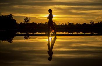 Silhouette of Man Standing on Lake at Sunset