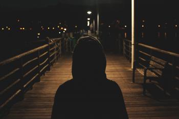 Silhouette of Person in Hoodie on Boardwalk at Night