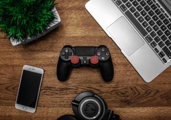Silver Macbook Beside Black Sony Ps4 Dualshock 4, Silver Iphone 6, and Round Black Keychain on Brown Wooden Table