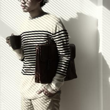 Standing Brunet Person Waring Eyeglasses and White Black Stripe Sweater Holding Mug and Briefcase