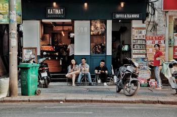 Three People Sitting on Chairs Outside Coffee & Tea House Near Motorcycles