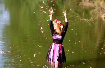 Time Lapse Photo of Woman Standing in Green Body of Water While Pouring Flower Petals on Air during Daytime