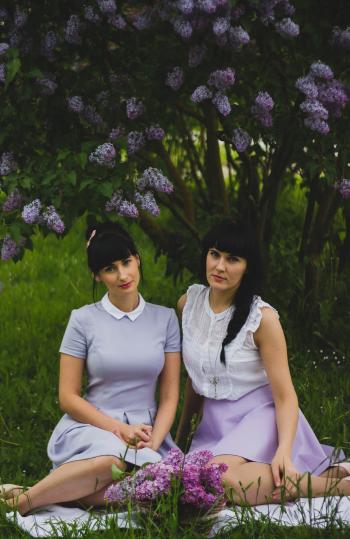 Two Women Wearing Purple Dress Sitting Side-by-side on Grass Field