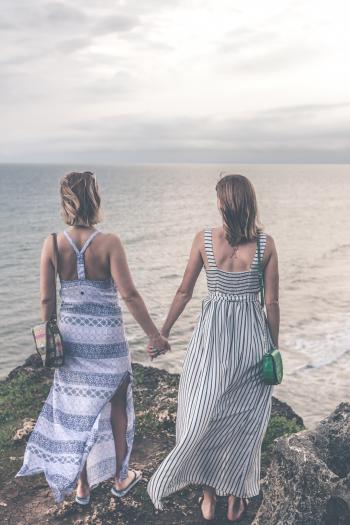 Two Women Wearing Sleeveless Dress Holding Each Others Hand on Cliff