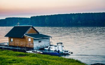 White Boat Beside Wooden House on Water Near Forest