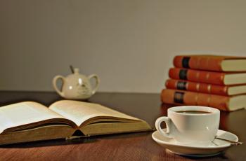 White Ceramic Teacup on Brown Wooden Table Beside Book