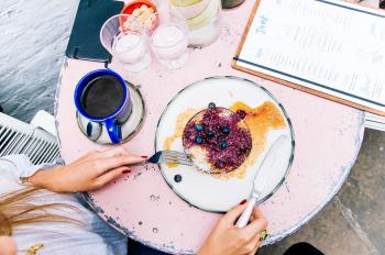 Woman Holding Spoon and Fork With Blackberries on Plate Beside Blue Ceramic Mug on White Wooden Table
