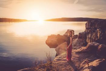 Woman in Black and Red Sleeveless Dress Standing Near Large Body of Water during Sunset