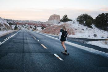 Woman in Black and White Long Sleeve Shirt Riding a Skateboard on a Freeway Road