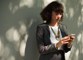 Woman In Black Blazer Holding A Smartphone While Standing Near Wall
