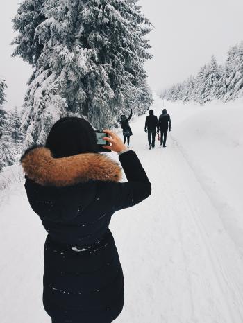 Woman in Black Coat Taking a Picture of Three Person in Front of Her While Walking Through Snow Field