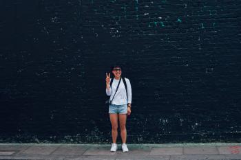 Woman in Blue Denim Shorts Standing in Front of Black Brick Wall