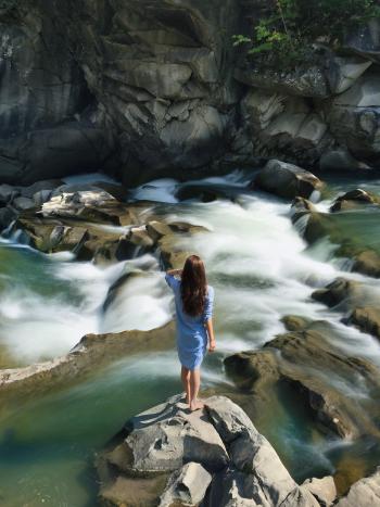 Woman in Blue Long-sleeved Dress Standing in Middle of Rock With Raging Water