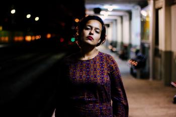 Woman in Brown and Purple Long-sleeved Shirt Standing Outside White Building during Nighttime