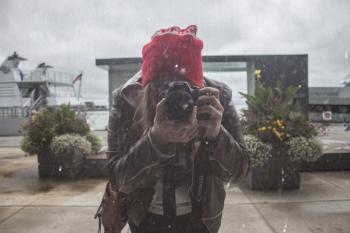 Woman in Brown Leather Jacket and Red Knit Cap Using Black Dslr Camera