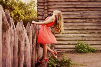 Woman in Orange Sleeveless Flare Dress Standing in Front of Wooden Fence