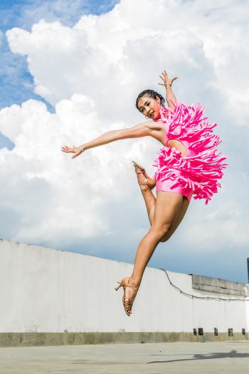 Woman in Pink Dress Doing Jump Shot While Extending Arms Under White Clouds