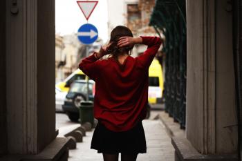 Woman in Red Sweater and Black Miniskirt Holding Hair Facing Road